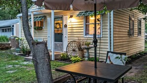 A wooden table with a brown umbrella, a house with a porch, and a garden with various plants. - Silver Heart Inn and Cottages (Independence)