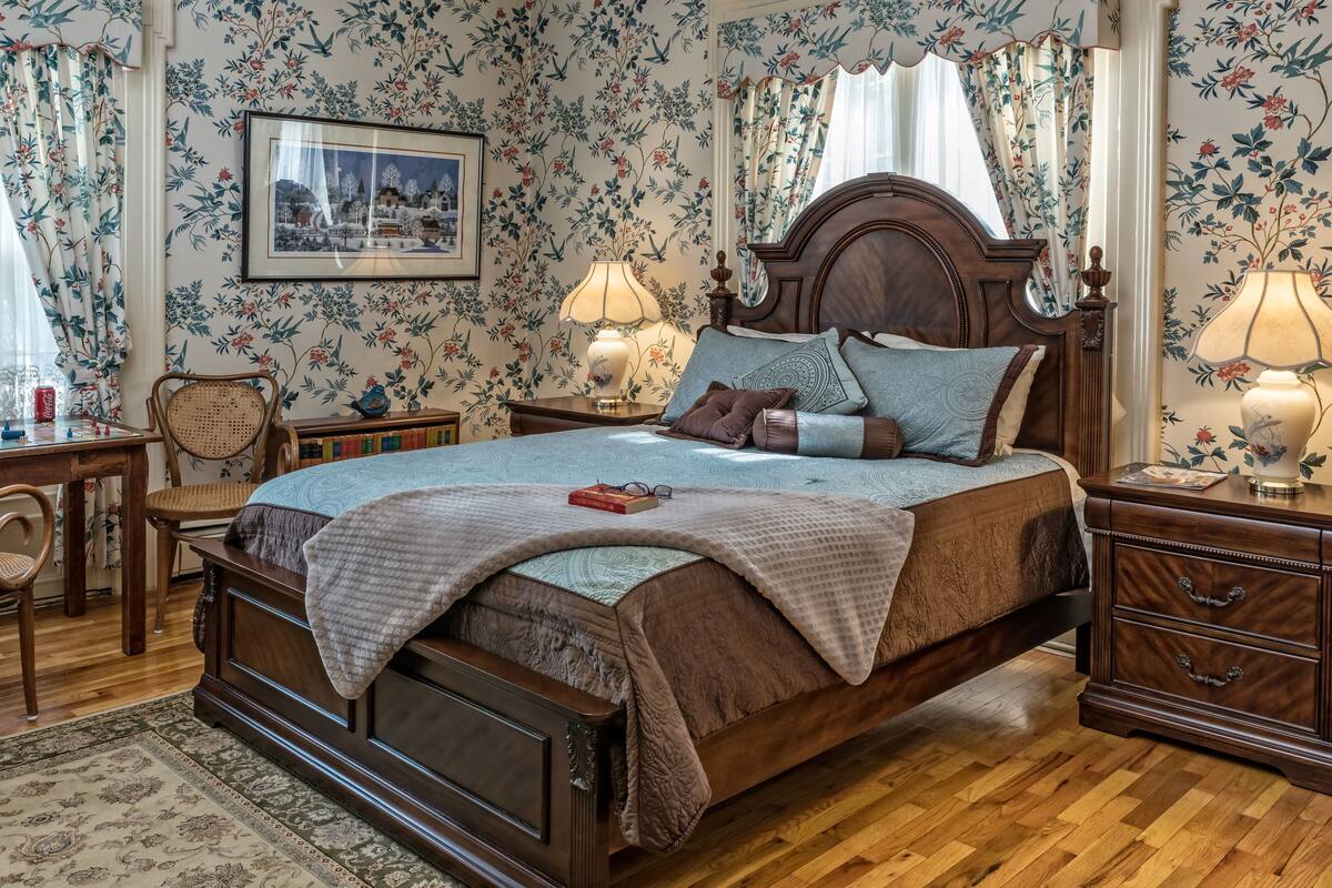 A traditional bedroom with a wooden bed, floral wallpaper, and a framed picture on the wall.
