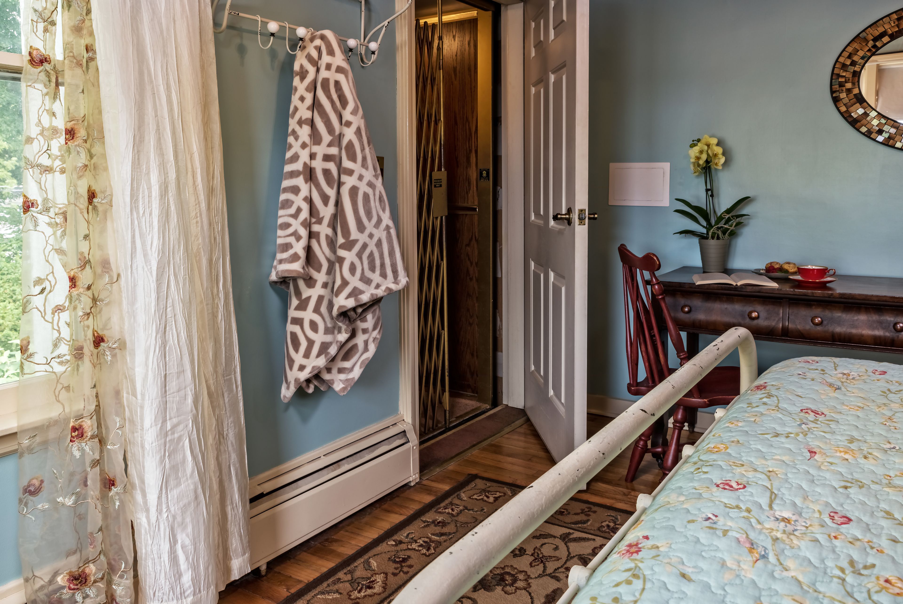 A bedroom with a bed, a wooden dresser, a chair, a potted plant, and a door leading to a bathroom.