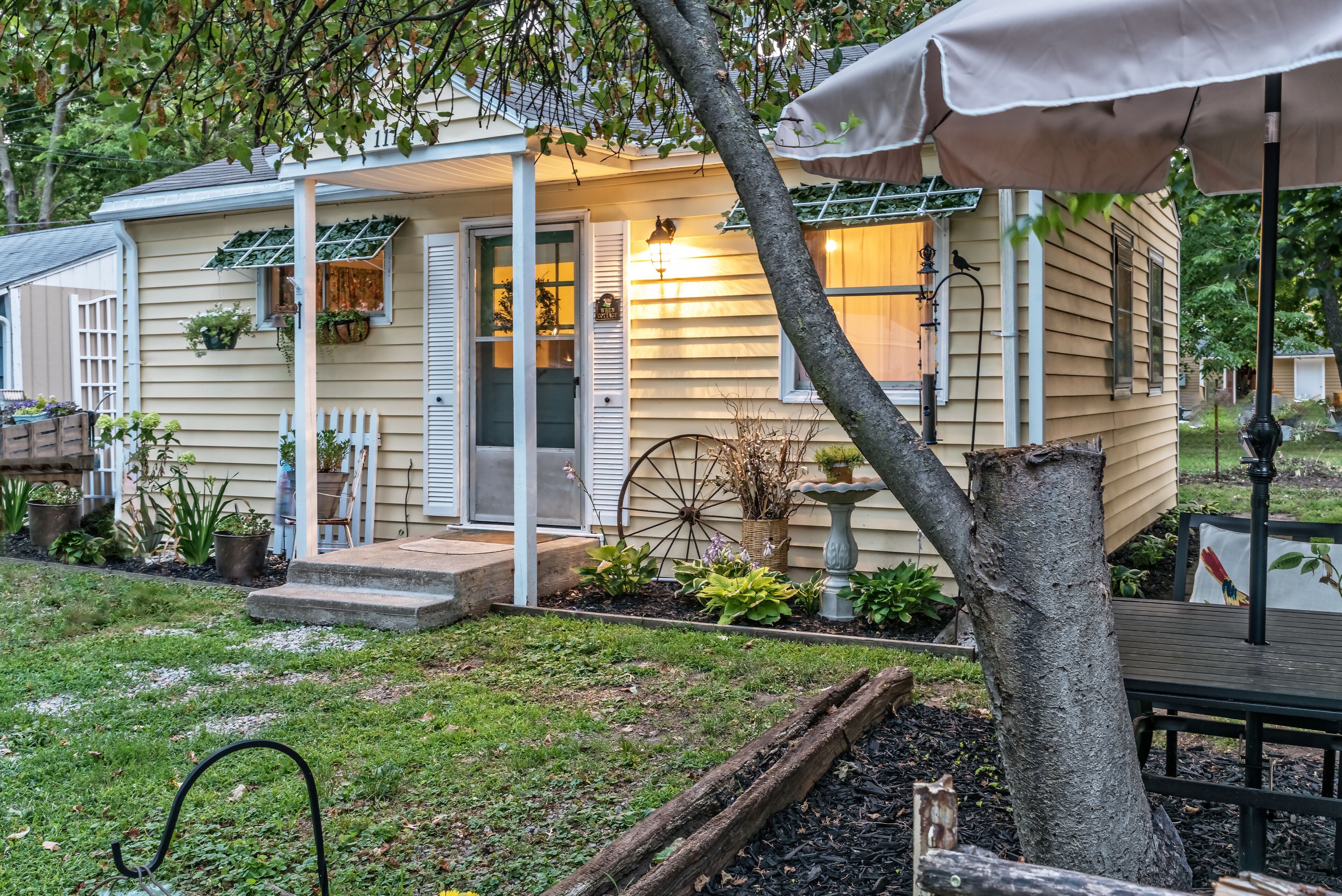 A house with a porch, a wheelbarrow, and potted plants.