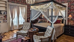 A bedroom with a four-poster bed, a sitting area with chairs, a small table with a wine glass, and a bookshelf. - Silver Heart Inn and Cottages (Independence)