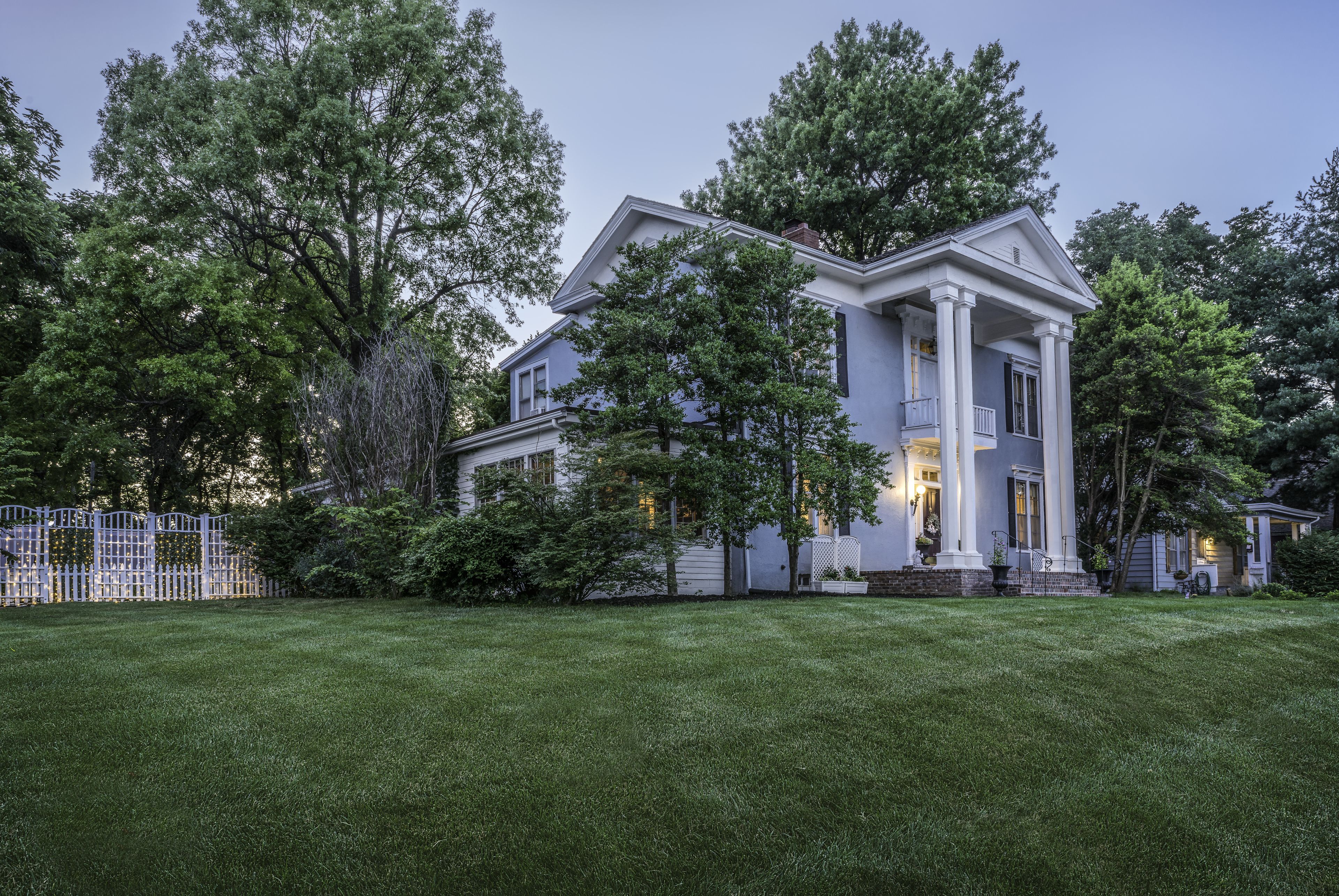 A large, two-story house with a prominent porch and columns, surrounded by a well-maintained lawn and trees.