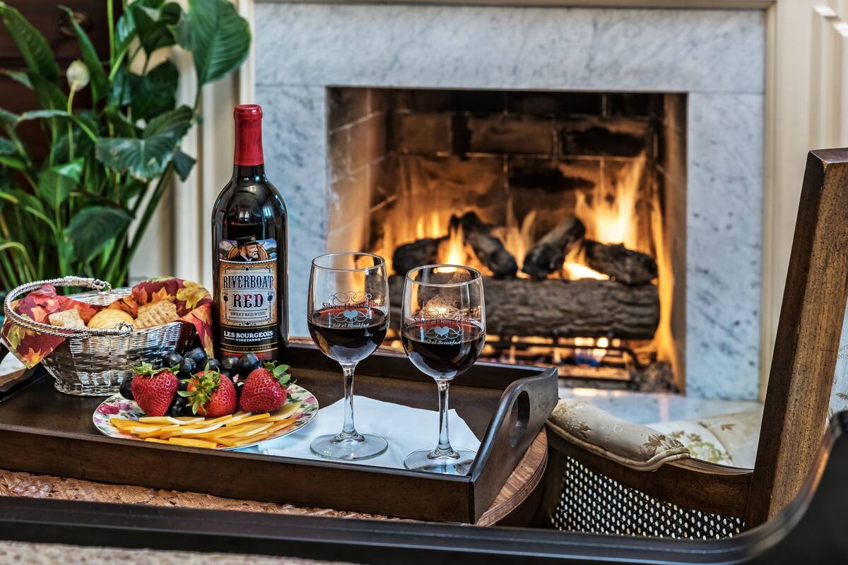 A tray with a bottle of red wine, two glasses, strawberries, blueberries, and crackers by a fireplace.