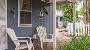 Un porche con dos sillas Adirondack blancas, una mesita y un velero decorativo colgado en la pared.