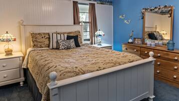 Quarto com cama, mesas de cabeceira, penteadeira, espelho e janela com cortinas.