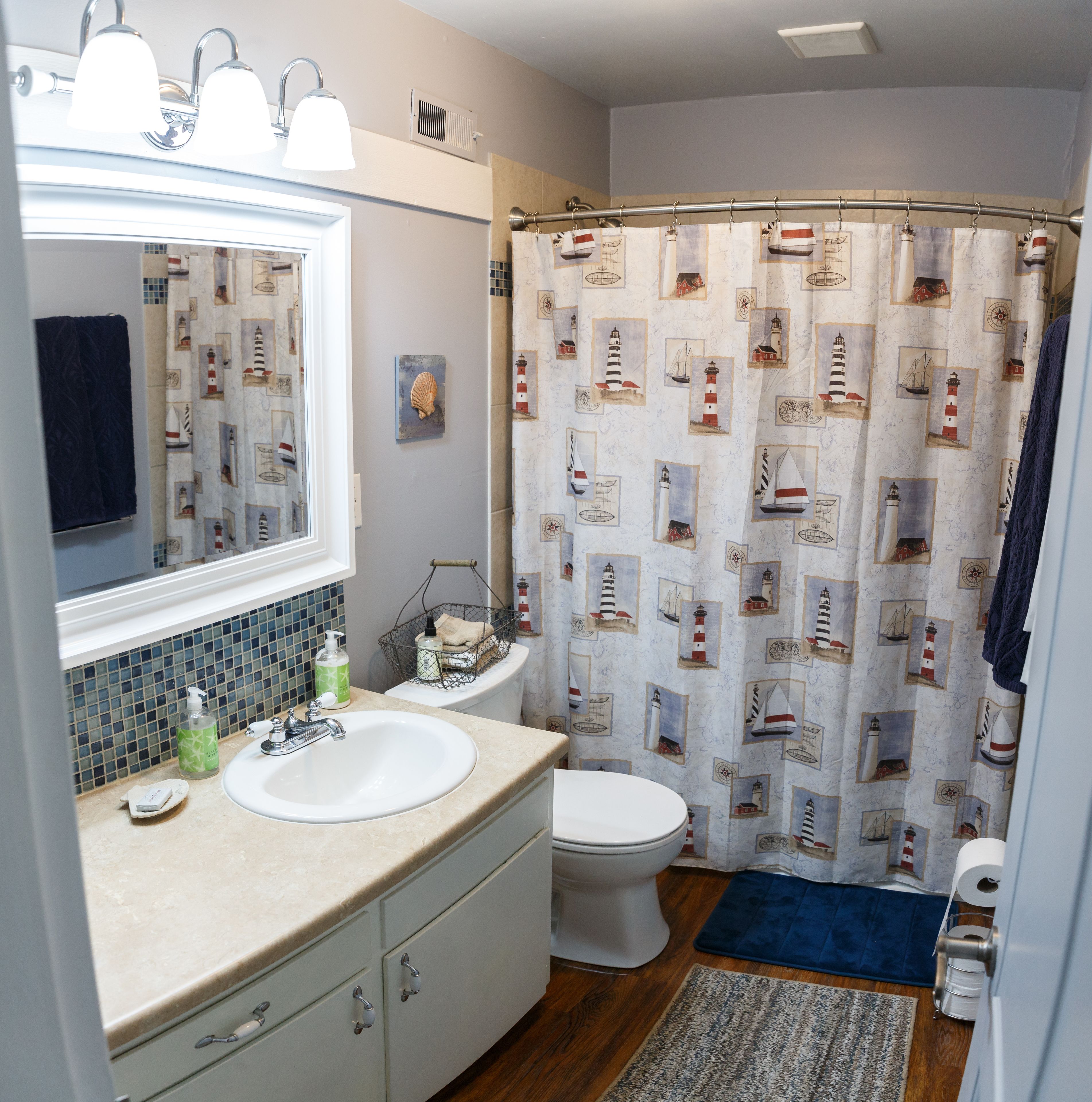 Une salle de bain avec un lavabo blanc, un miroir, des toilettes et un rideau de douche orné de motifs marins.