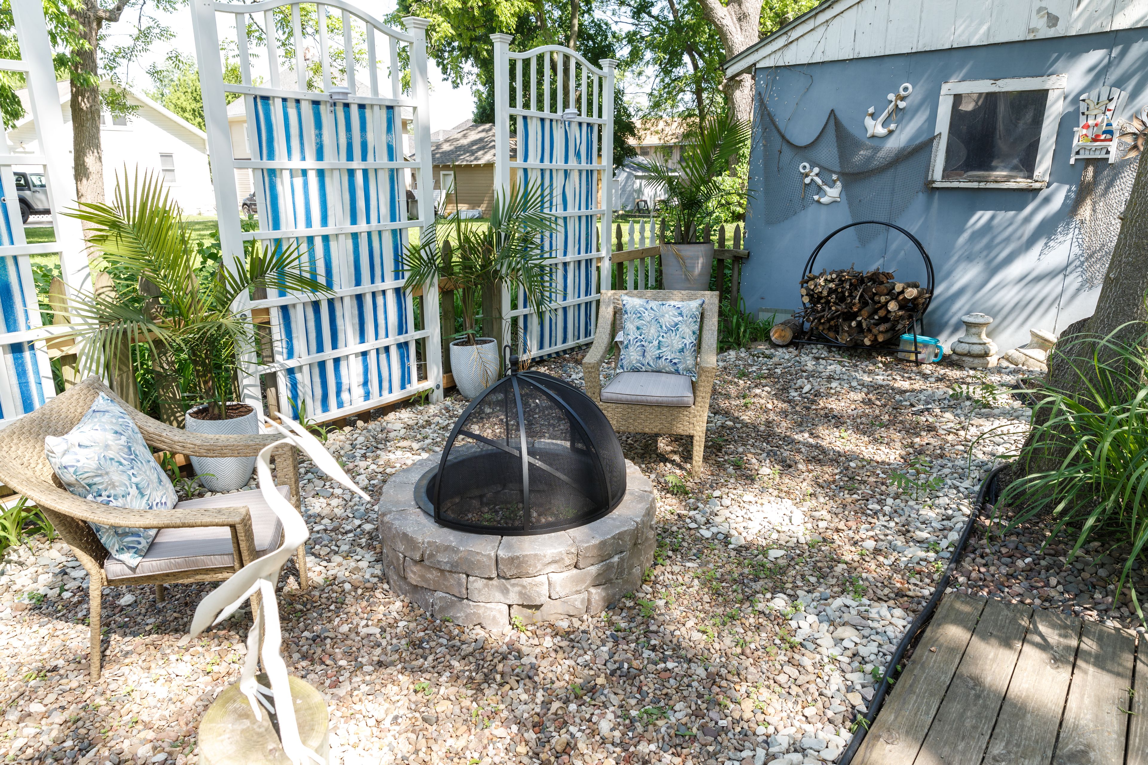 A backyard with a fire pit, outdoor seating, and a blue building with nautical decorations.