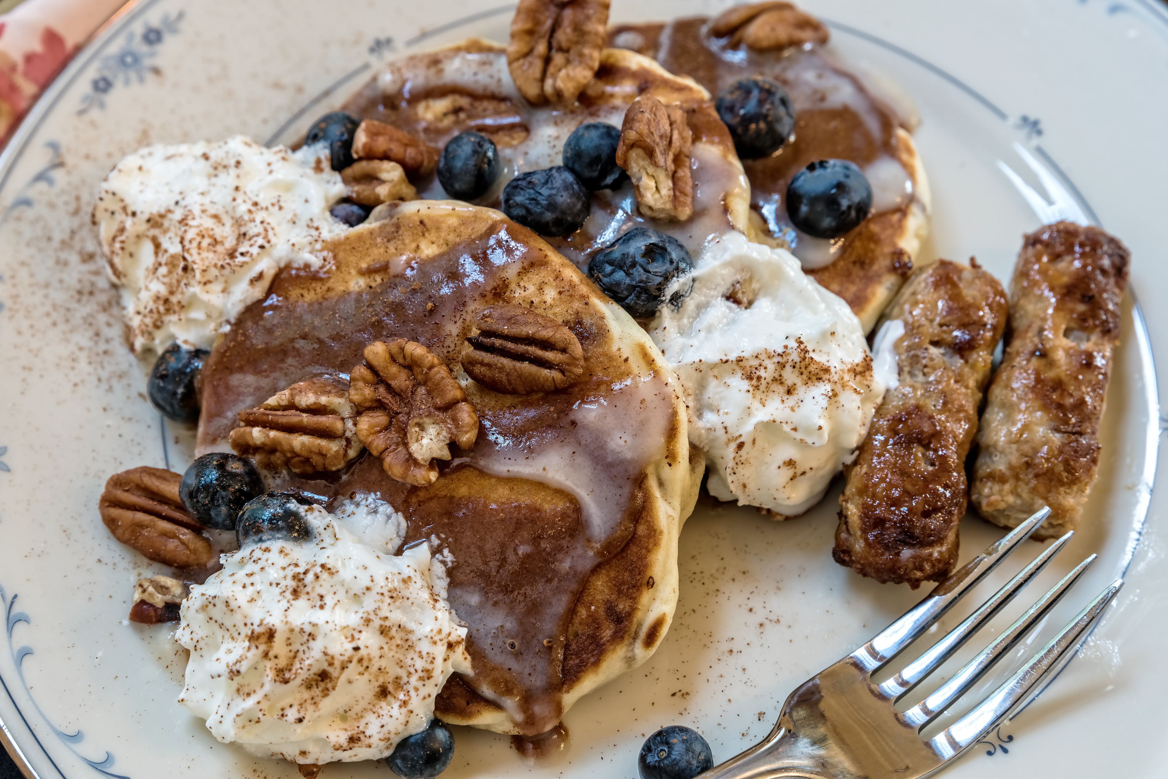 Una porción de tortitas con arándanos, nueces pecanas y almíbar.