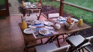 Una mesa de desayuno para dos personas, con platos, tazas, una jarra de jugo y una cesta de croissants.