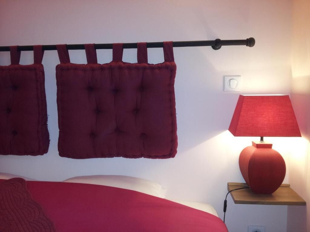 A bedroom with a bed, a nightstand, a lamp, and a wall-mounted curtain rod with two curtains.