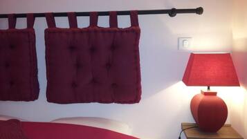 A bedroom with a bed, a nightstand, a lamp, and a wall-mounted curtain rod with two curtains.
