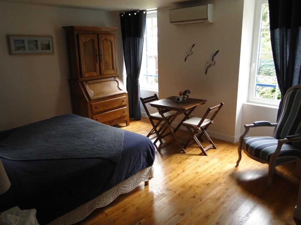A bedroom with a bed, a wooden dresser, a dining table with chairs, and a window with curtains.