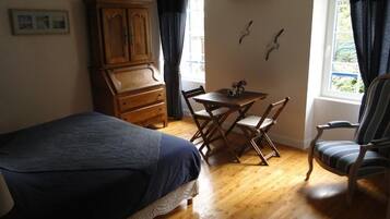 A bedroom with a bed, a wooden dresser, a dining table with chairs, and a window with curtains.