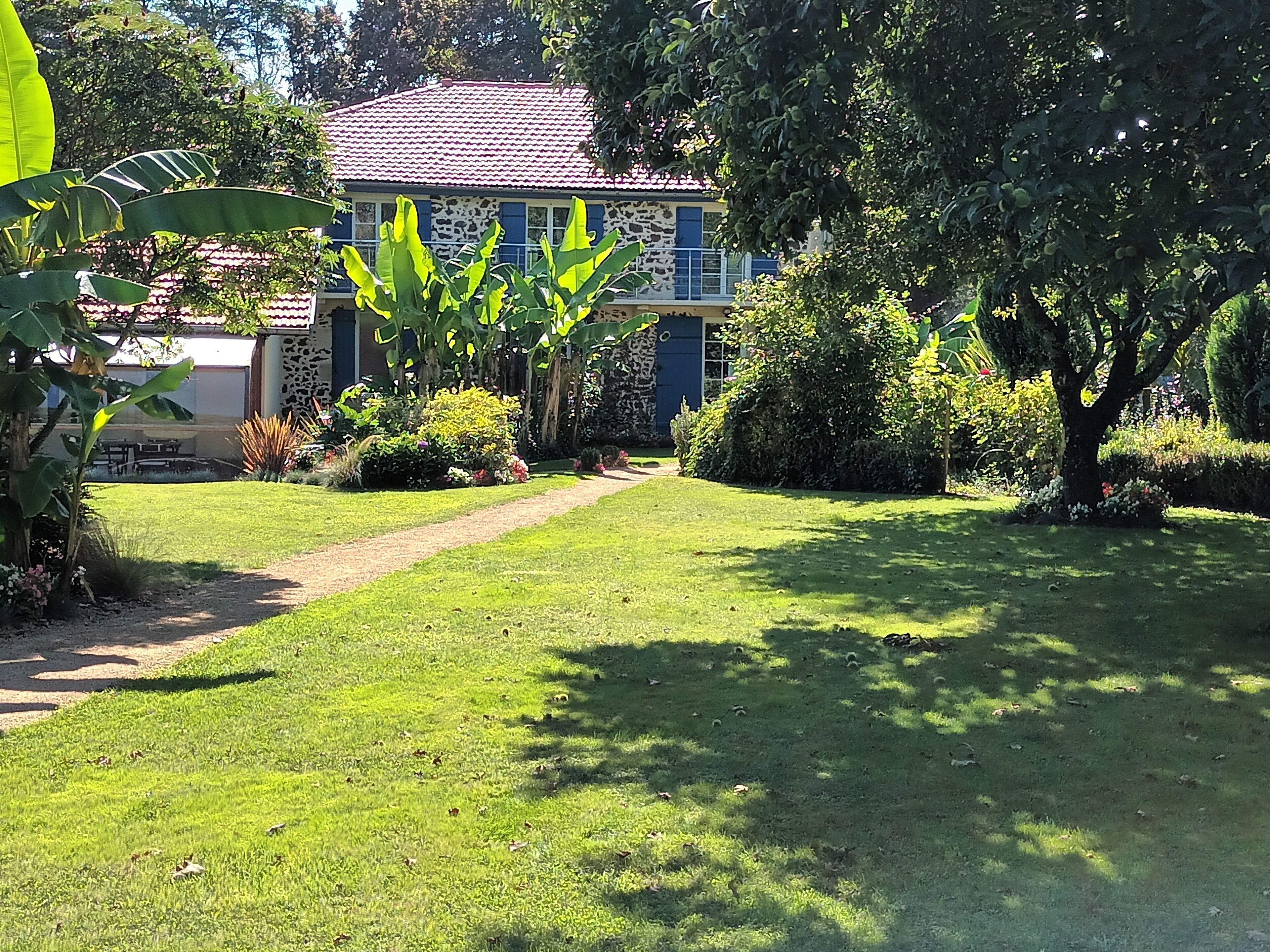 A well-maintained garden with a paved pathway leading to a house with a stone facade and blue shutters.