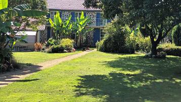 A well-maintained garden with a paved pathway leading to a house with a stone facade and blue shutters.