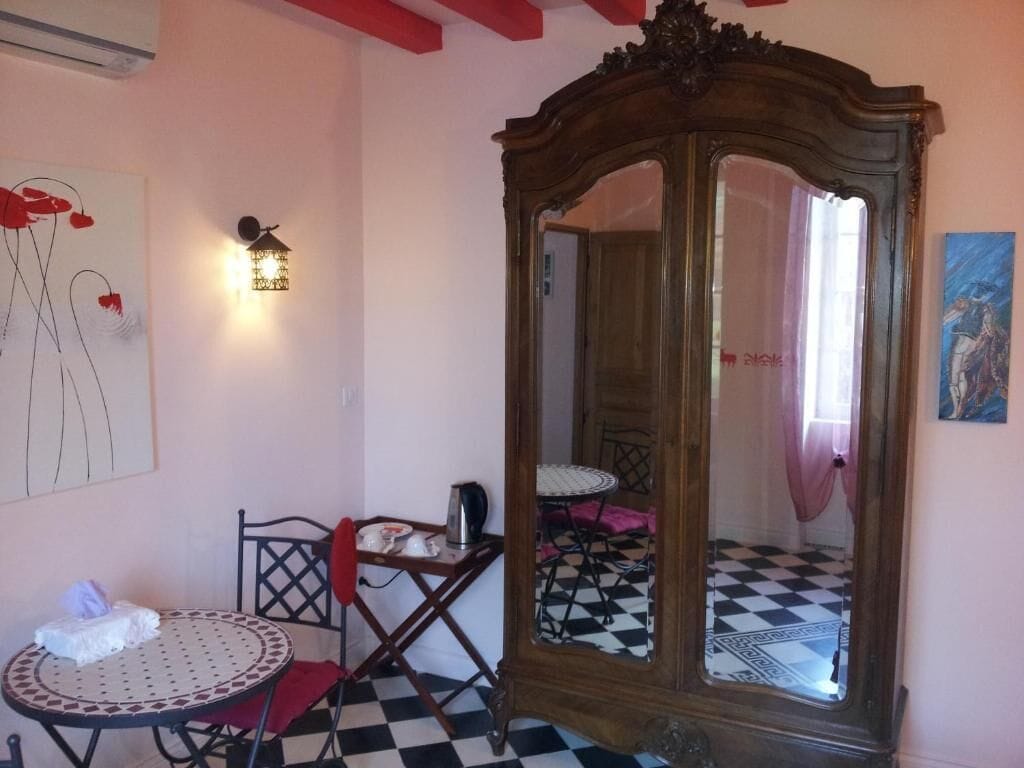 Une pièce avec un sol à carreaux, une table ronde avec une chaise, un luminaire fixé au mur et un grand miroir avec un cadre en bois.