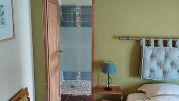 A bedroom with a wooden bed, a nightstand with a lamp, a bench, and a door leading to a bathroom with a tiled floor.