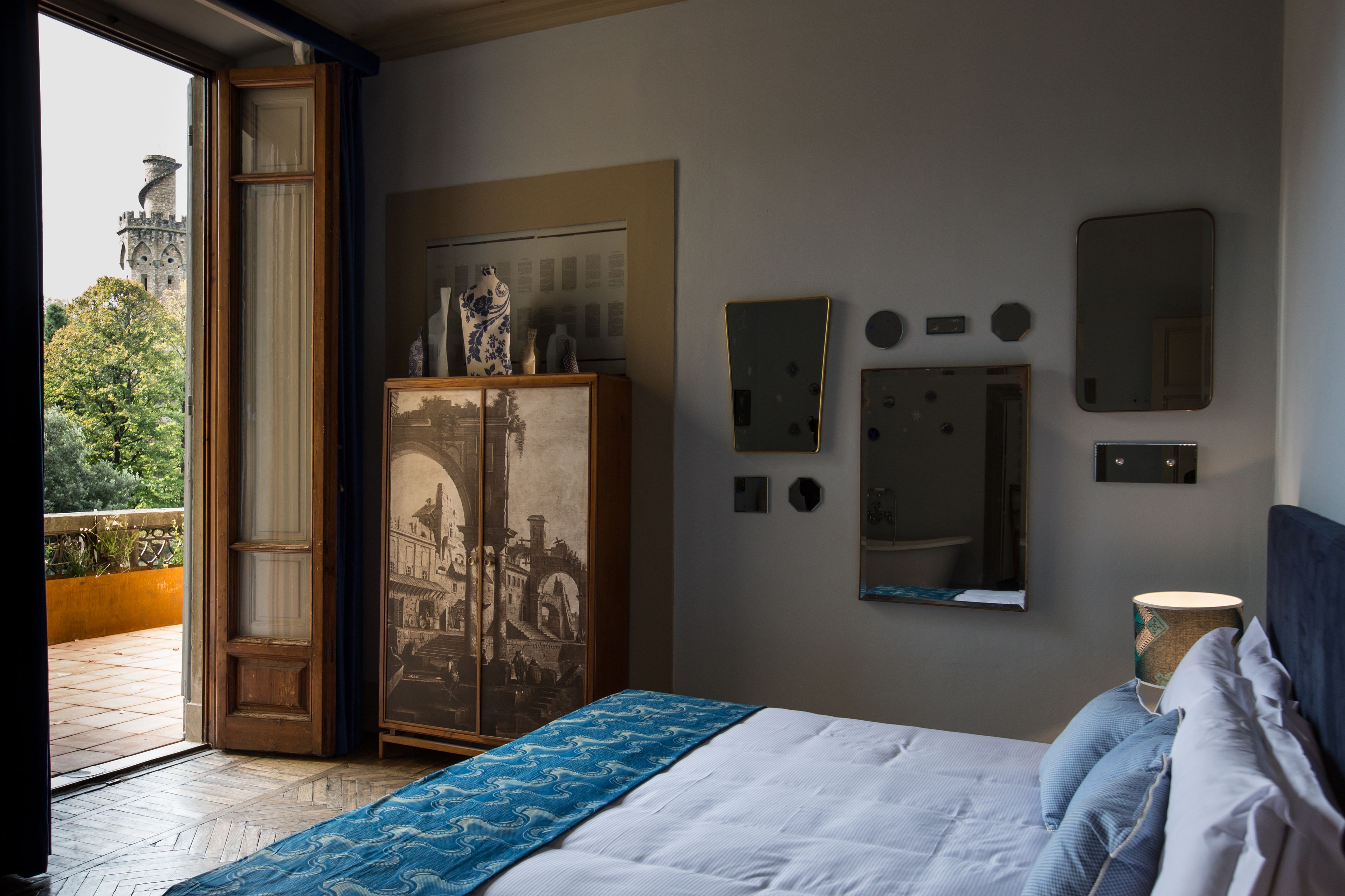 A bedroom with a bed, a wardrobe, and a large window with a view of a castle.