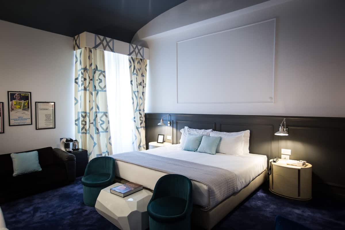 A hotel room with a large bed, two chairs, a desk, a nightstand, and a lamp.