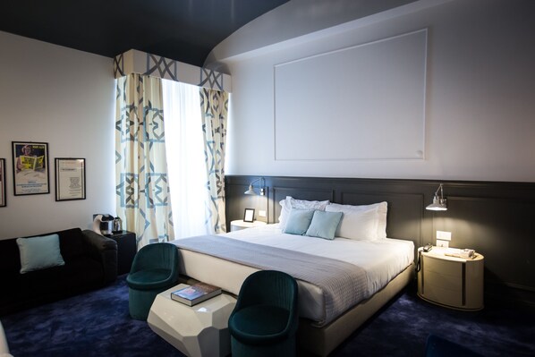 A hotel room with a large bed, two chairs, a desk, a nightstand, and a lamp.