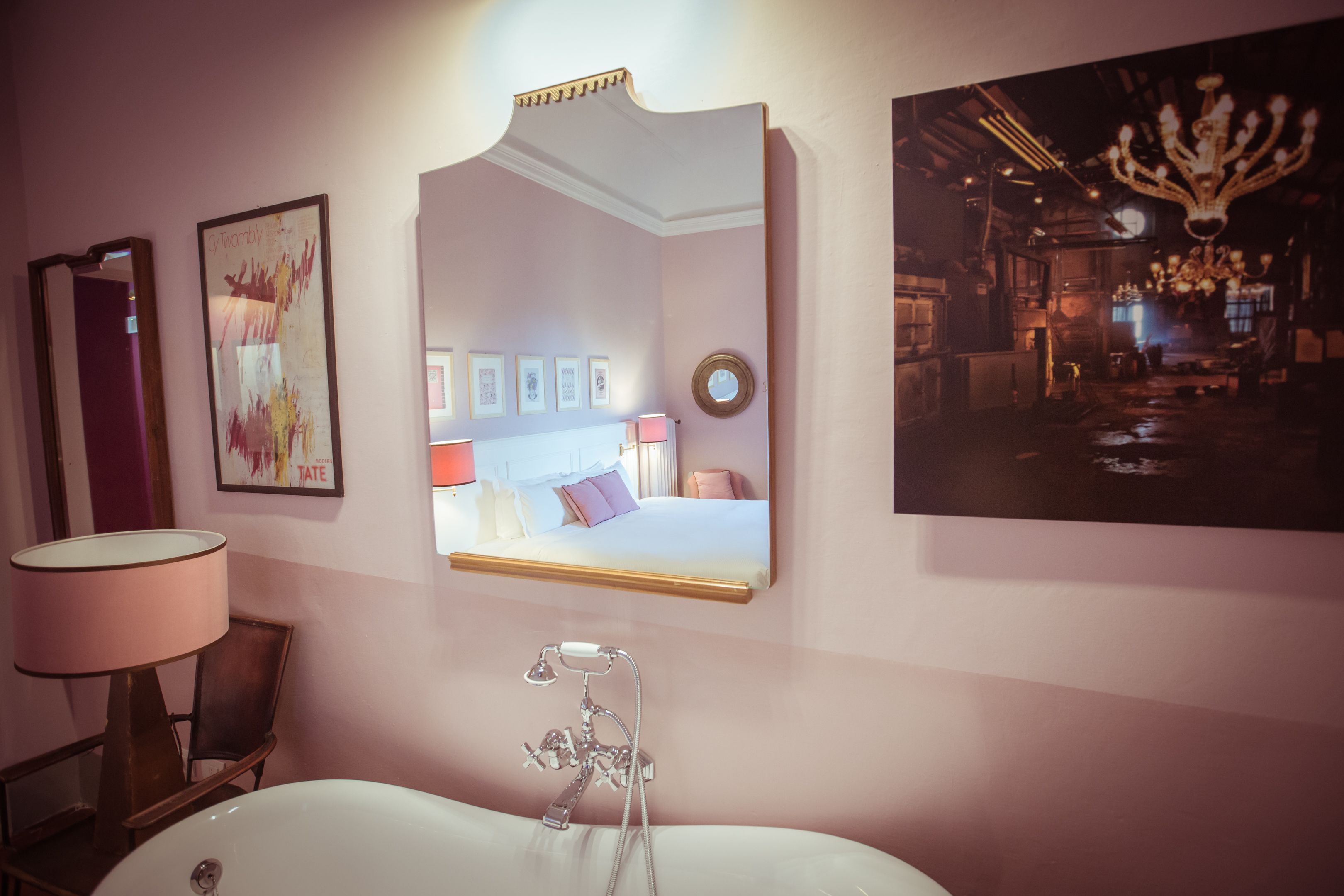 A bathroom with a large mirror, a bathtub, a chair, and a wall-mounted lamp.