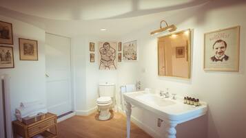 A bathroom with a white sink, toilet, and wooden floor. There are framed pictures on the walls and a mirror above the sink.