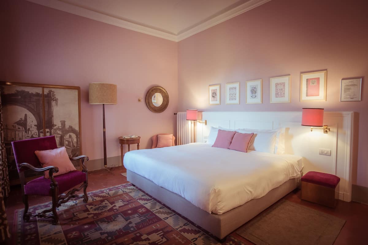 A bedroom with a large bed, a chair, a rug, and framed pictures on the wall.
