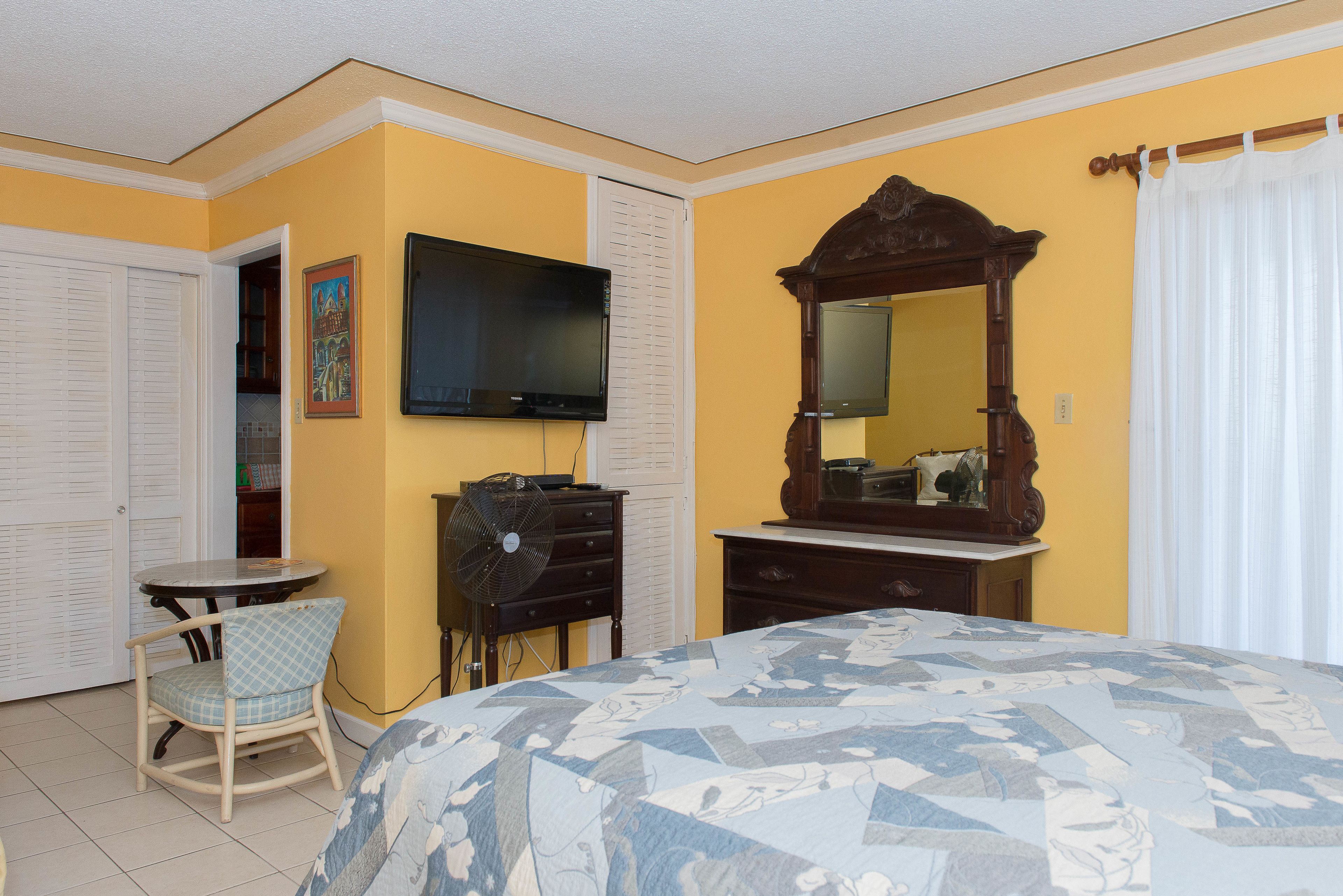 Una habitación de hotel con una cama, televisor, cómoda, silla y espejo.