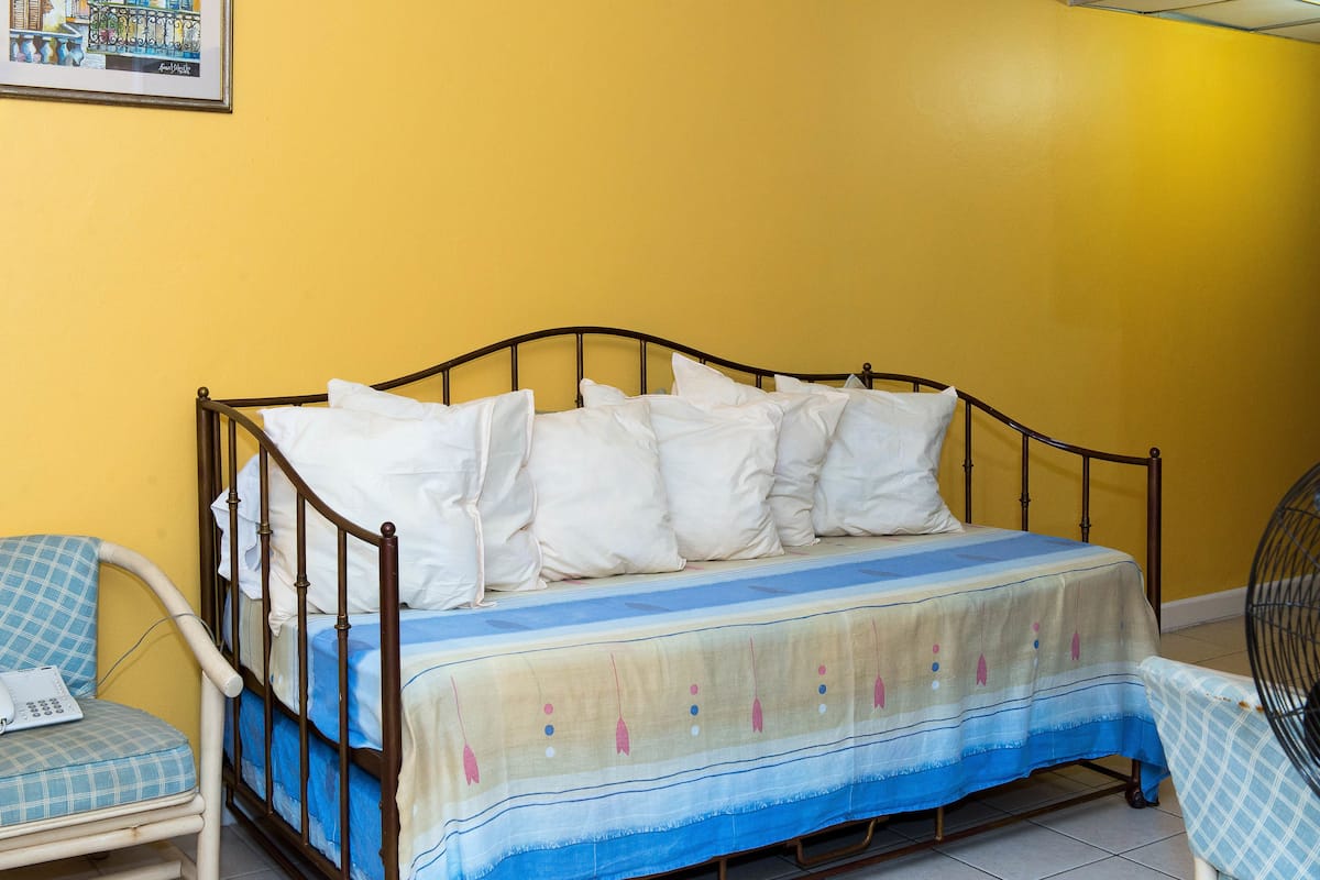 A bed with a blue and white bedspread, a chair with a checkered cushion, and a wall-mounted picture.