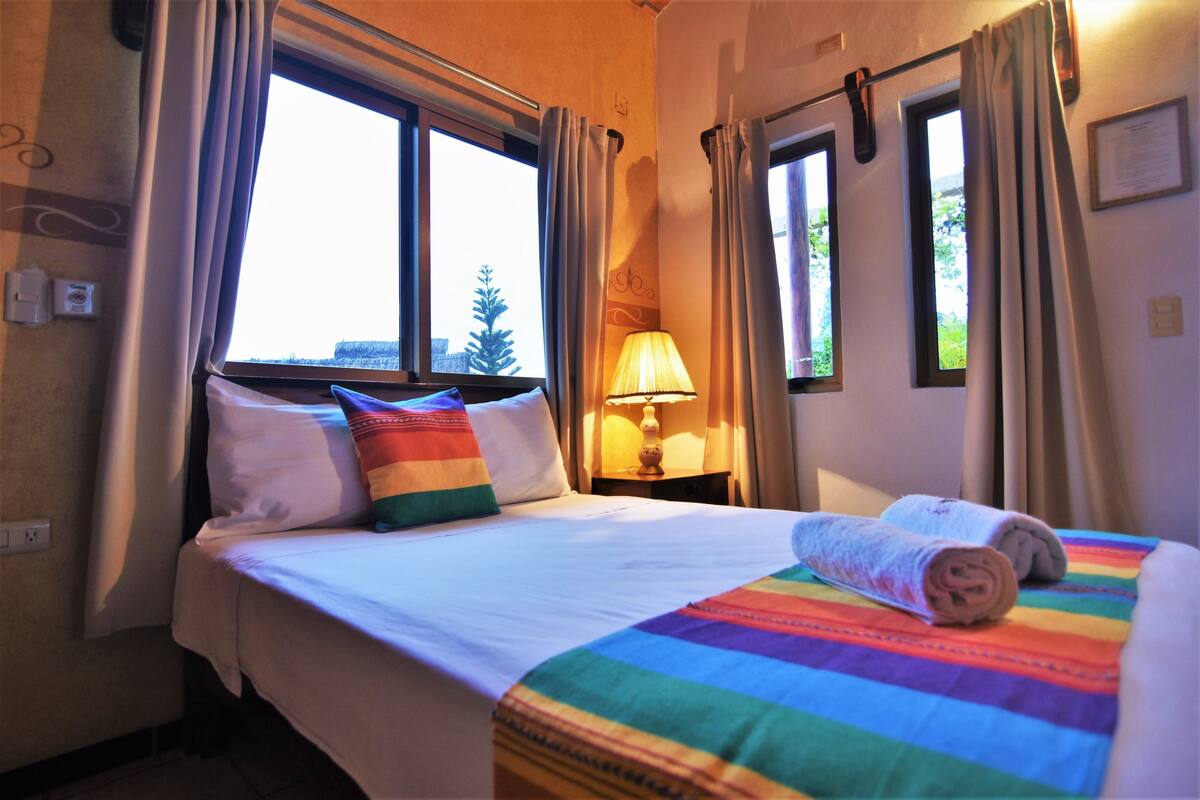 Ein Hotelzimmer mit Bett, Lampe und fensterbepflanzten Fenstern.
