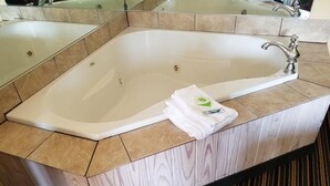 A large, rectangular bathtub with a wooden vanity and a mirror above it.