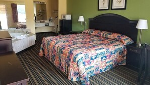 A hotel room with a bed, a desk, a chair, a mirror, a sink, and a lamp.