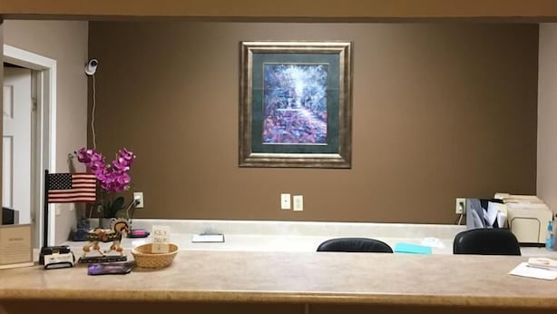 A reception desk with a framed painting above it, a small American flag, and a decorative plant.