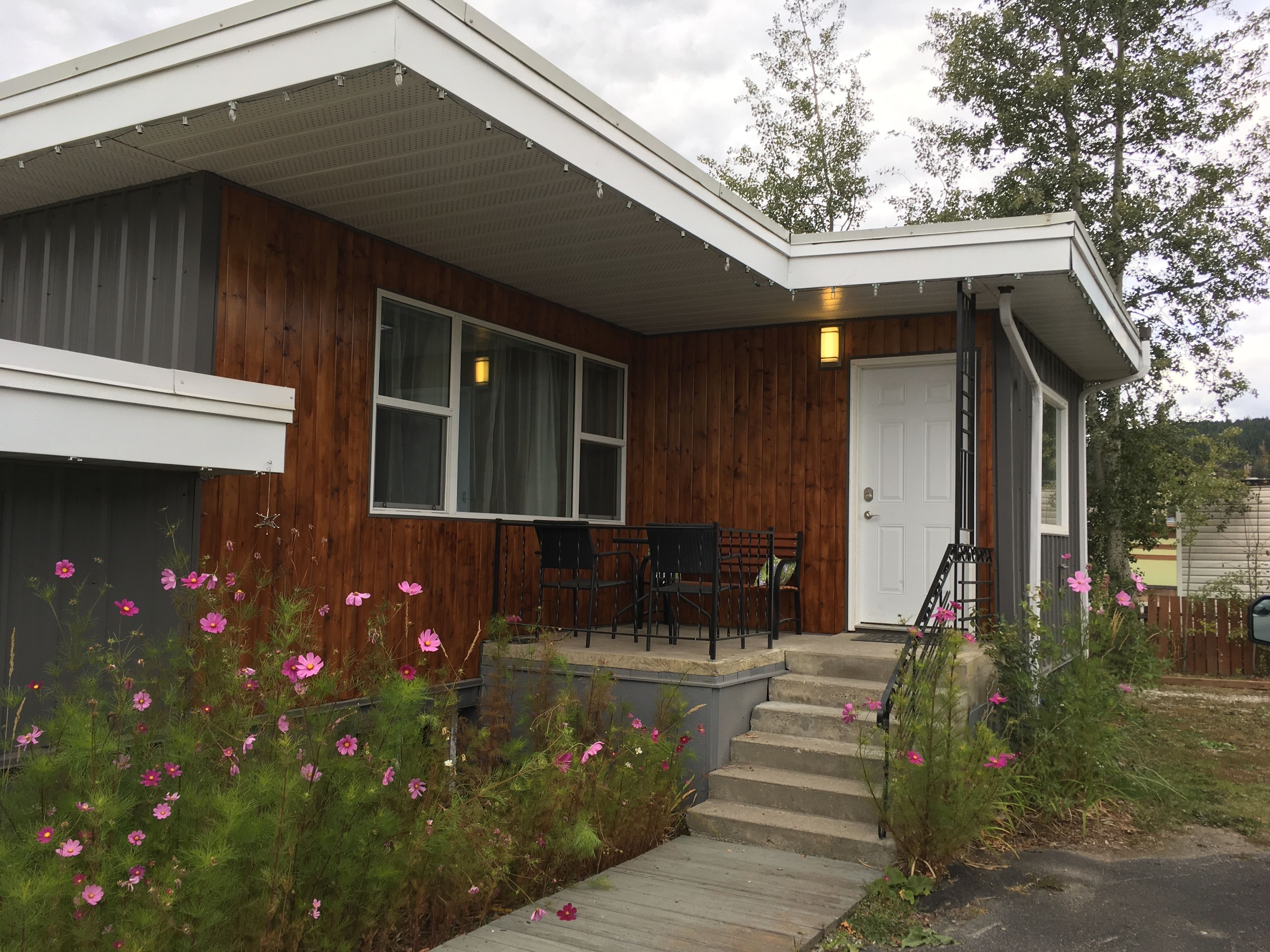 A modern house with a wooden exterior, a porch with chairs, and a staircase leading to the door.