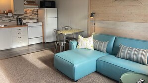 A modern kitchen with white cabinets, a refrigerator, and a microwave. There is a dining table with chairs and a blue sofa with striped pillows. - Pinewood Inn (Golden)