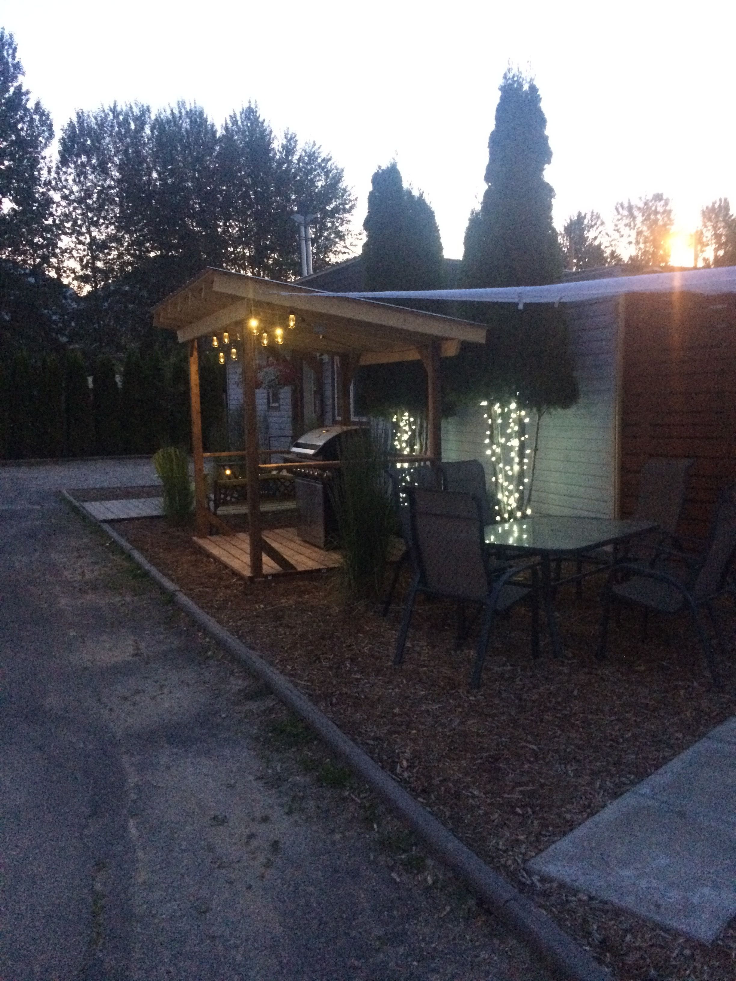 Un espace extérieur aménagé en terrasse, doté d’une pergola en bois, d’un barbecue et d’une table avec des chaises.