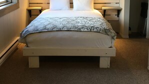A neatly arranged bedroom with a bed, bedside tables, a wall-mounted lamp, and a decorative plant. - Pinewood Inn (Golden)