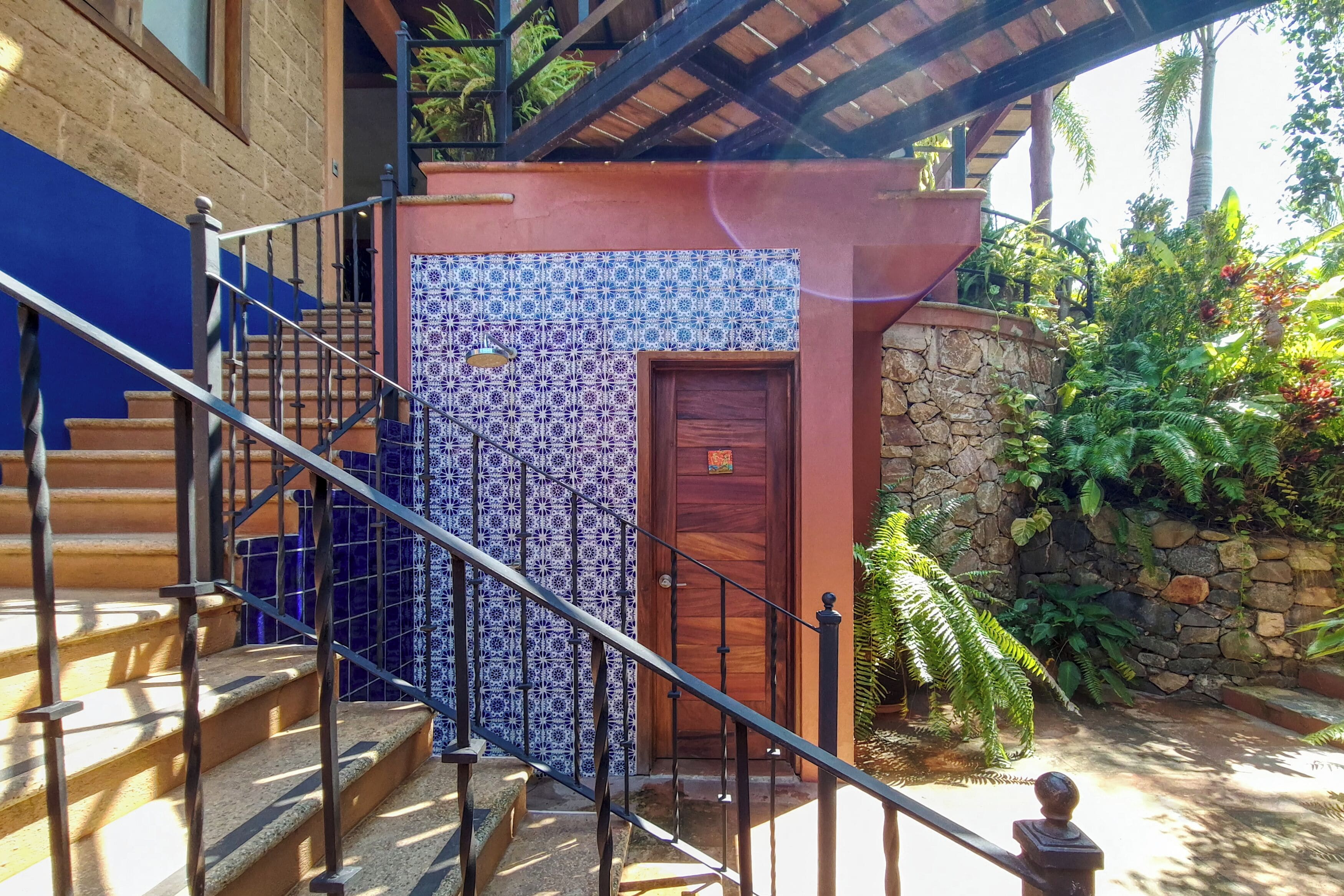 A staircase with a blue and white patterned wall, a wooden door, and a stone wall with greenery.