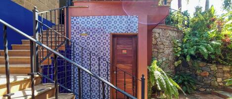 A staircase with a blue and white patterned wall, a wooden door, and a stone wall with greenery.