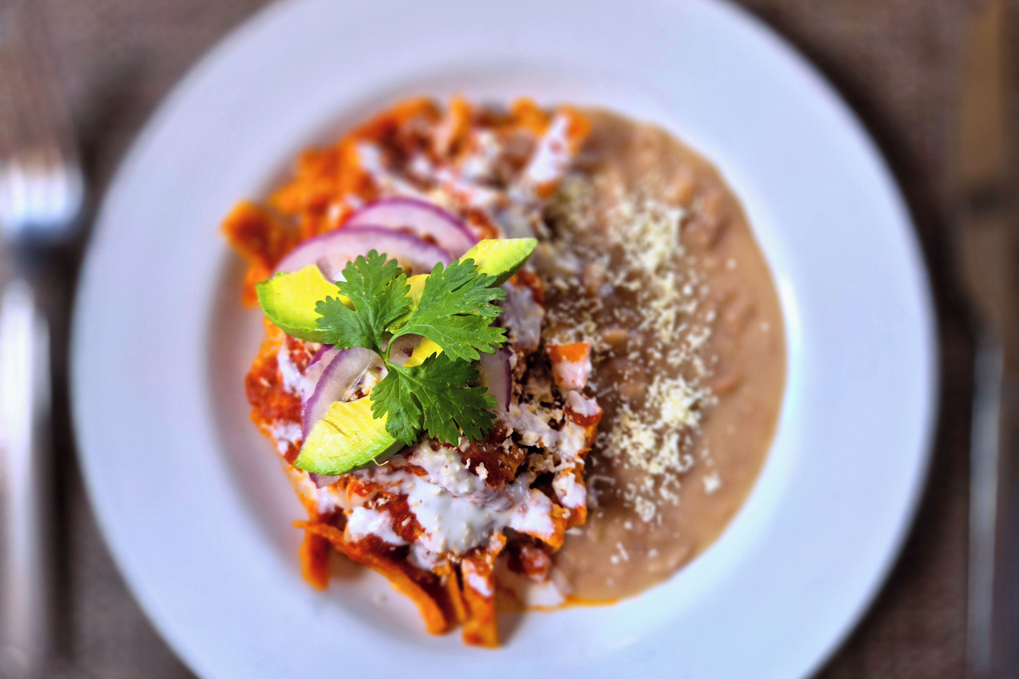 A plate of enchiladas with a side of refried beans, garnished with avocado, red onion, and cilantro.