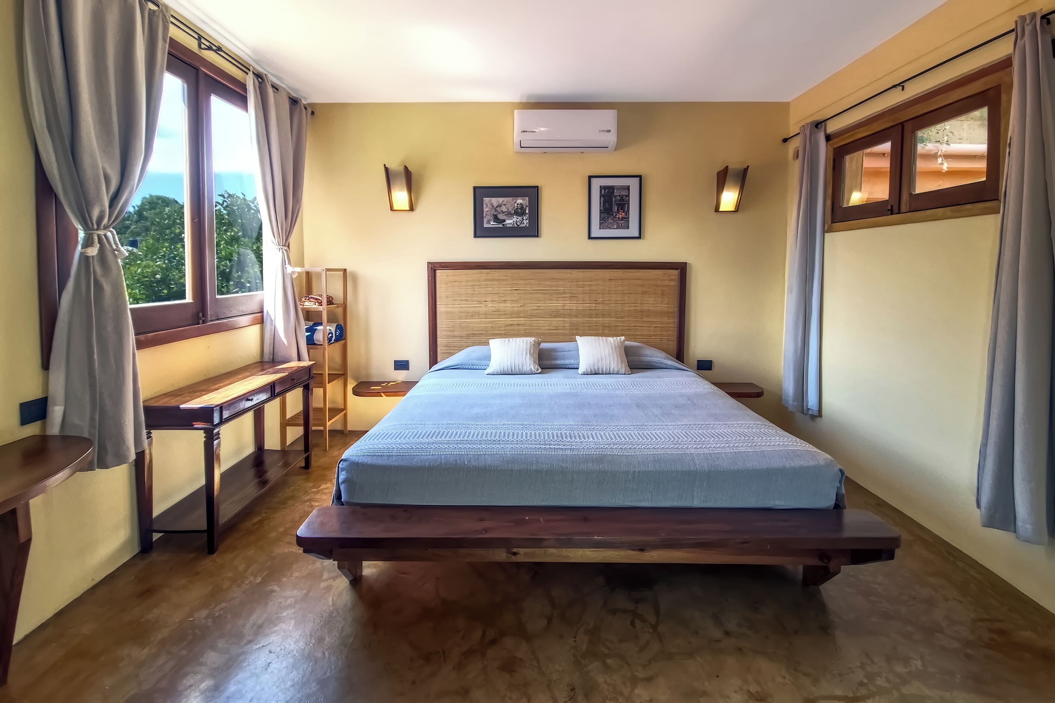 A bedroom with a wooden bed, a bedside table, a bench, and two wall-mounted lights.