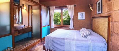 Un dormitorio con cama, ventana con cortinas, baño con lavamanos y techo de madera.