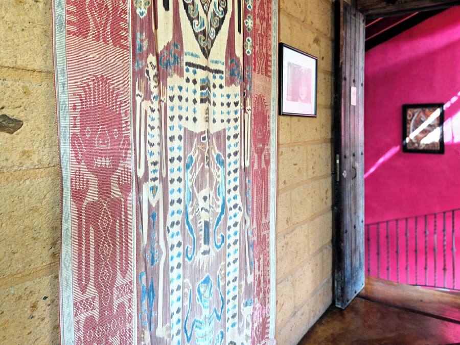 A hallway with patterned textiles on the walls and a bright pink wall on the right.