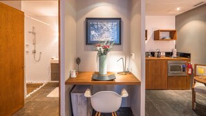 A compact, modern room with a wooden desk, a white chair, a framed artwork on the wall, and a small kitchenette with a microwave and toaster. - Suites at Sapphire Ocean Club (Puerto Vallarta)