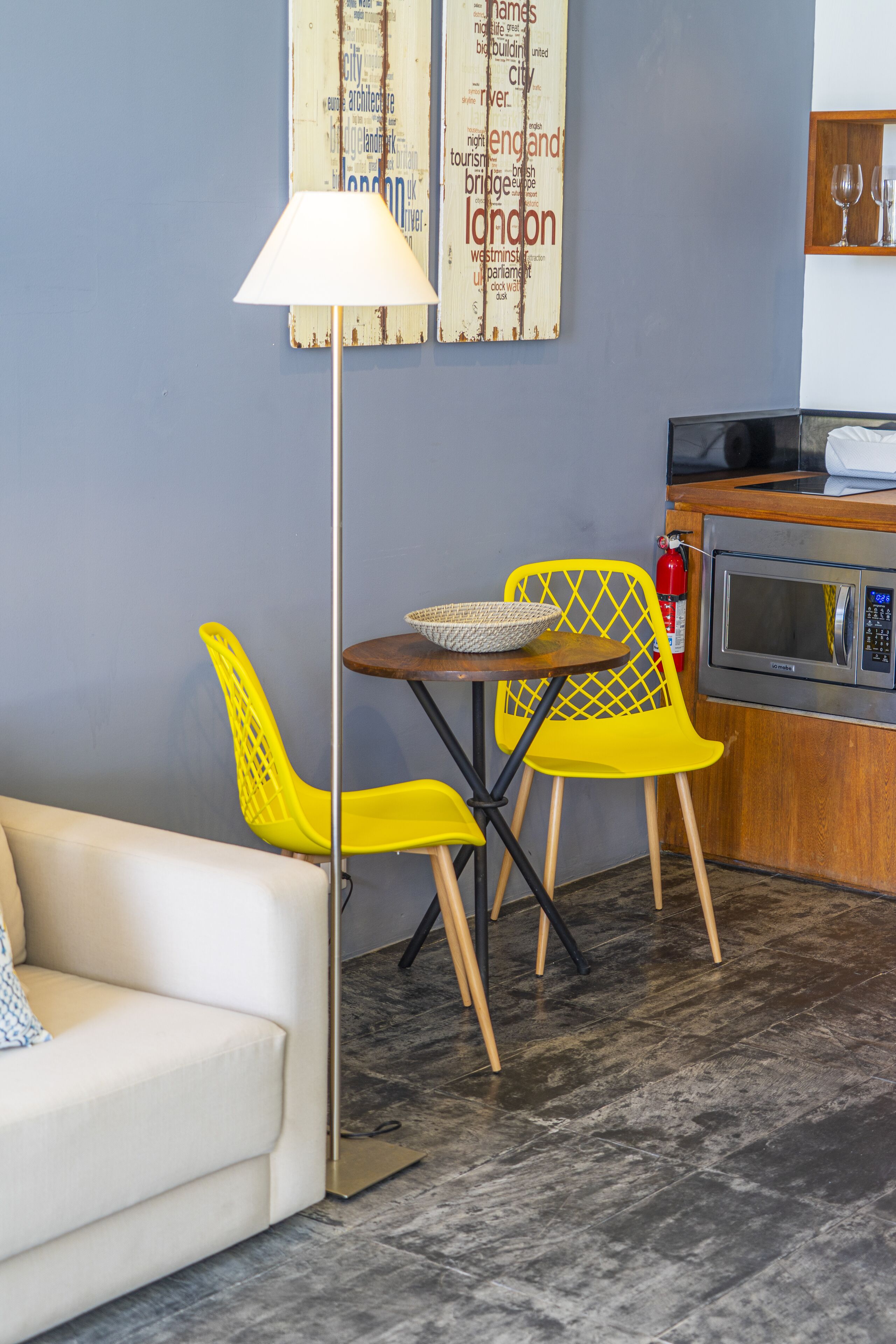 Un espacio habitable compacto con un sofá, una mesa de comedor con dos sillas, una lámpara de pie y una cocina con microondas.