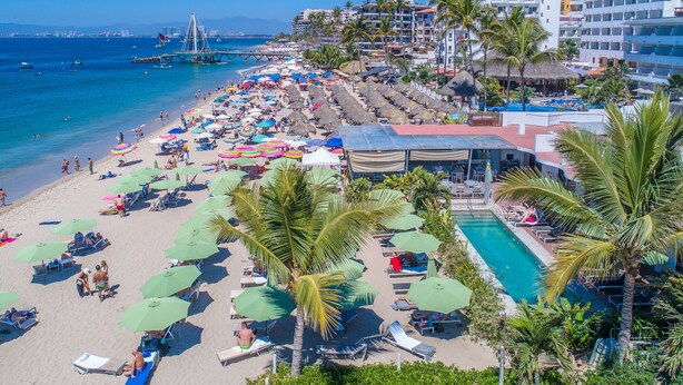 A beach resort with a pool, sun loungers, umbrellas, and a view of the ocean. - Suites at Sapphire Ocean Club (Puerto Vallarta)