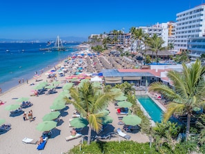 A beach resort with a pool, sun loungers, umbrellas, and a view of the ocean.