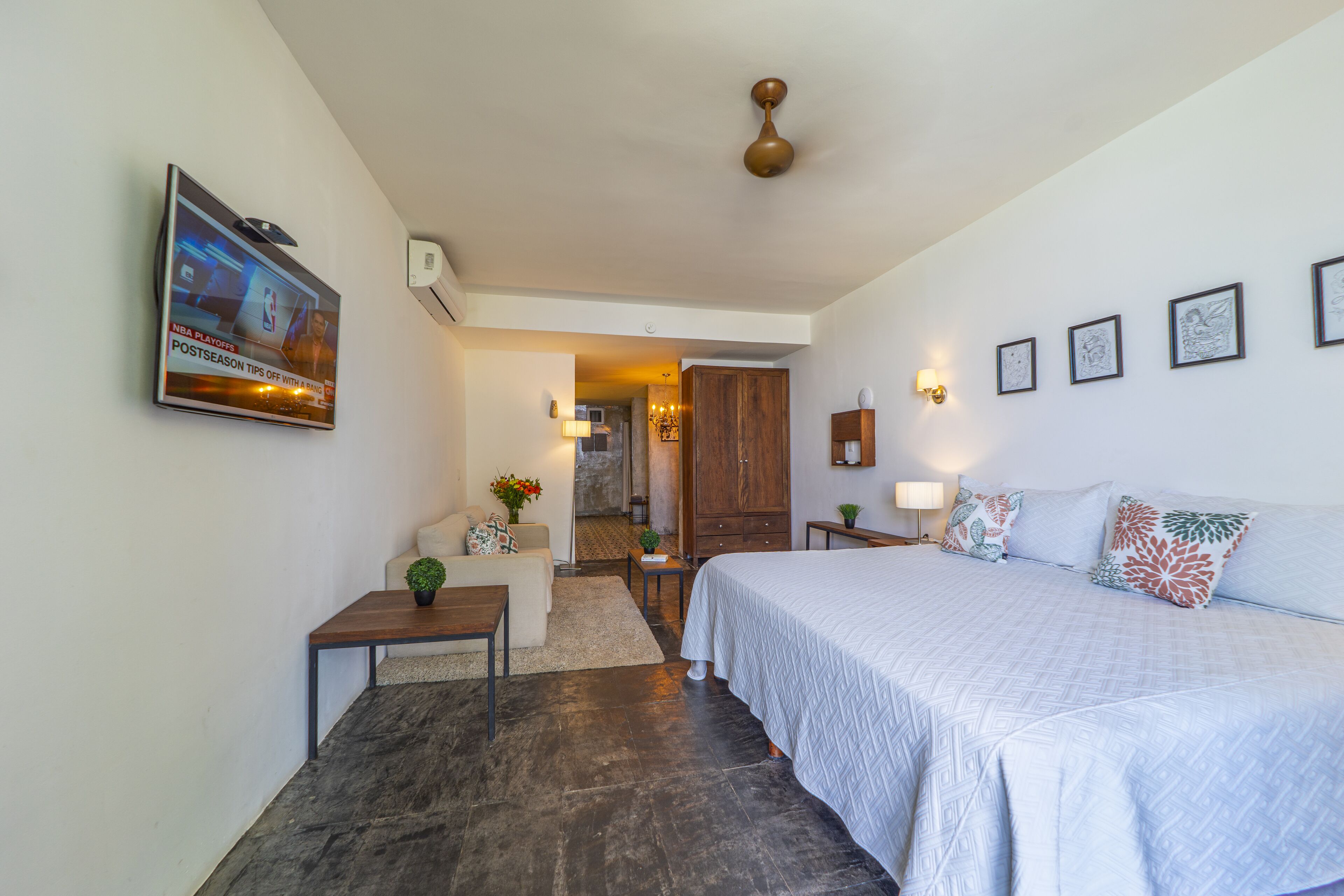 Une chambre à coucher comprenant un lit, un bureau, une chaise, un téléviseur fixé au mur et une porte donnant sur une autre pièce.