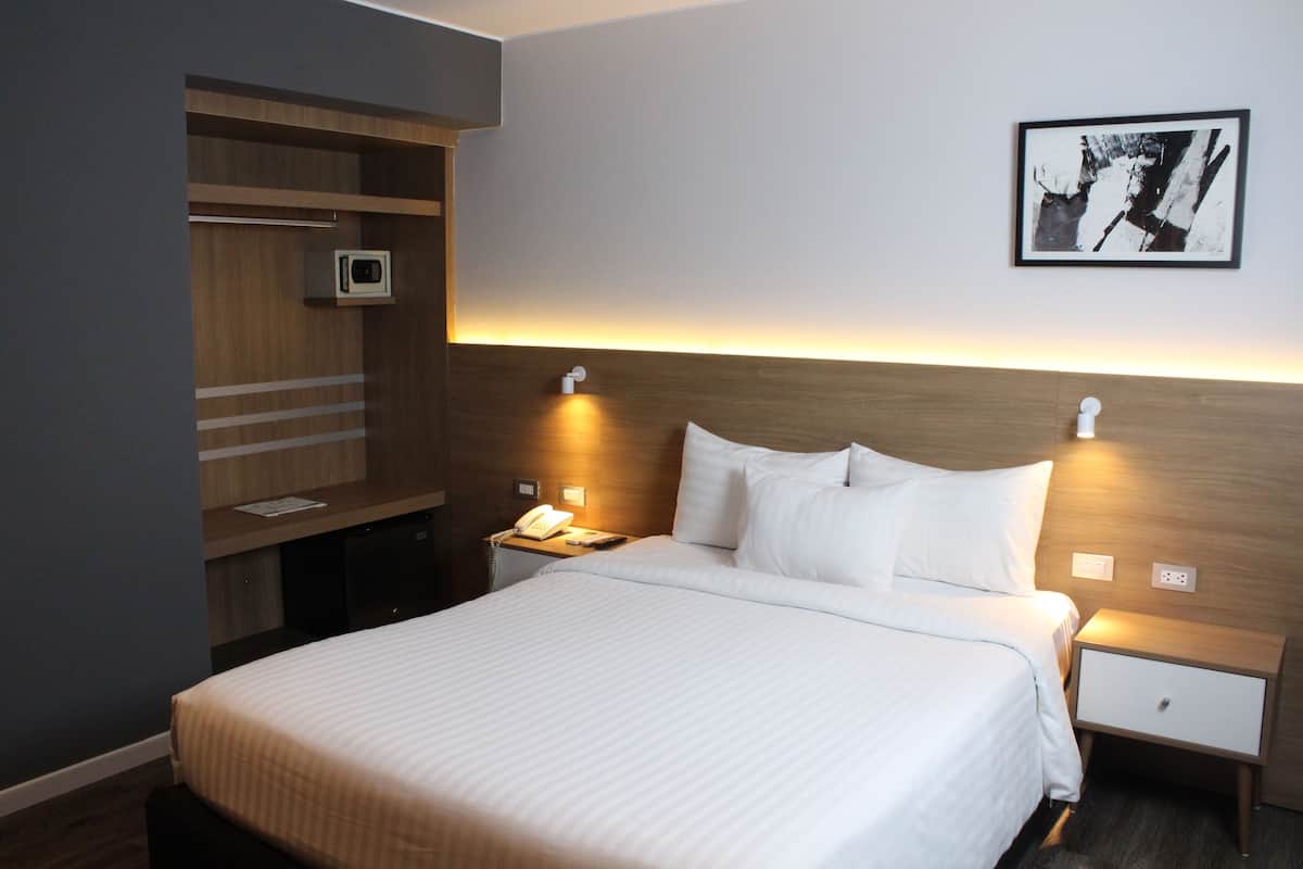 Een hotelkamer met een groot bed, nachtkastjes, een bureau, een stoel, een televisie en een ingelijste foto aan de muur.