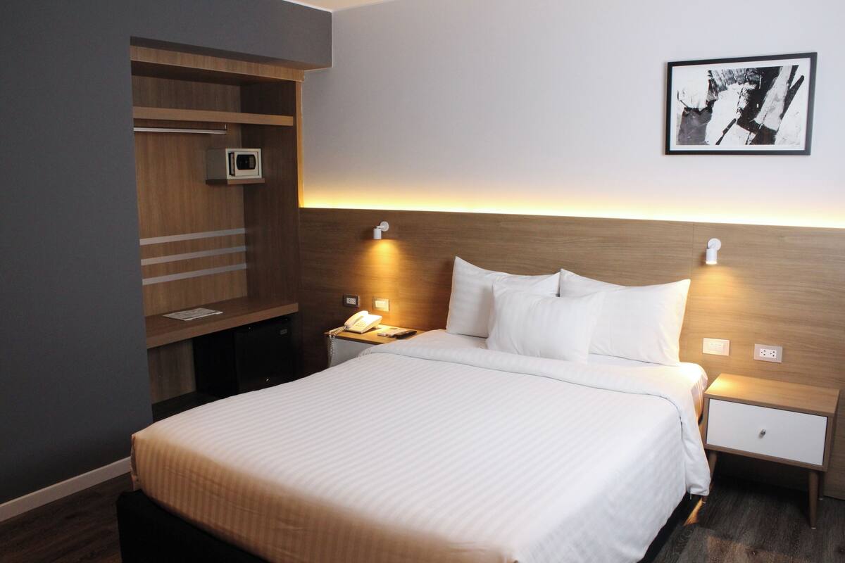 Hotelkamer met een bed, nachtkastjes, een bureau met stoel, een wandtelevisie en een ingelijst schilderij aan de muur.